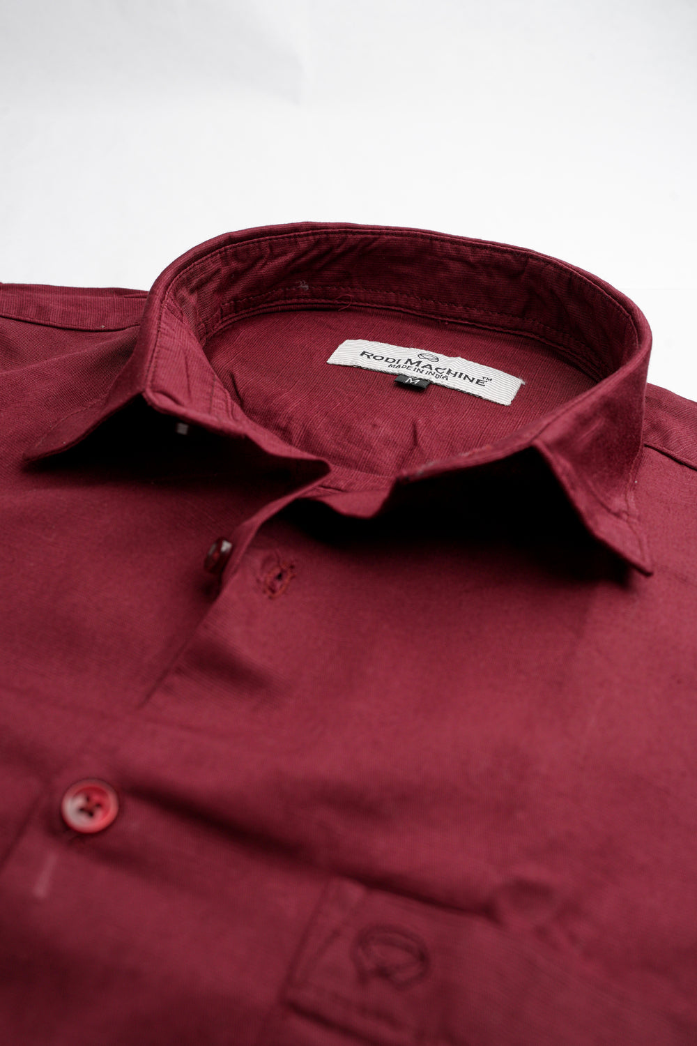 Close-up of a Maroon colour Rodi Machine shirt with a brand label on a white background