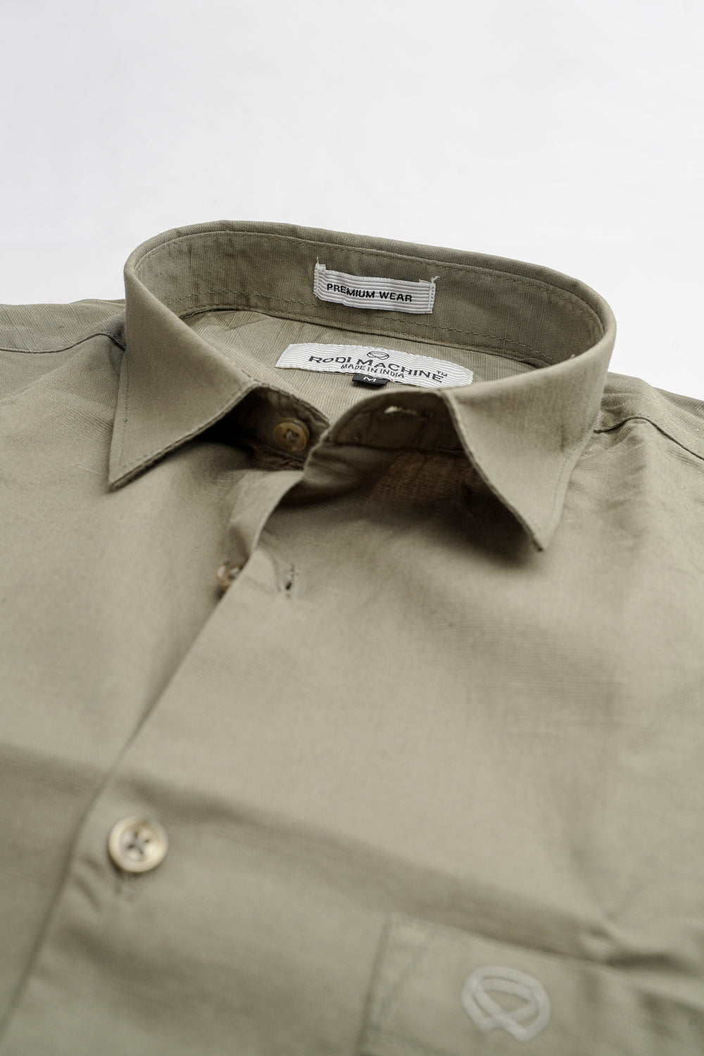 Close-up of a Olive Green Rodi Machine shirt with collar and button details on a light gray background